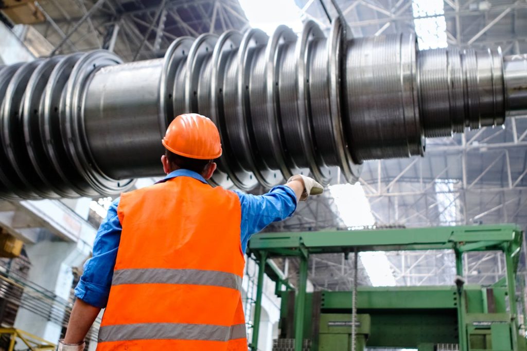 man-wearing-orange-hard-hat-2760241 Engineer in high visibility vest and hard hat inspecting large machinery in factory setting.